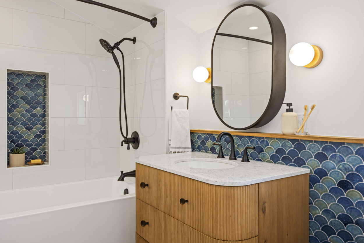 A bathroom with a rounded mirror, a vanity with rounded corners, and a backsplash with rounded tiles represents the 2025 design trends of curves. 