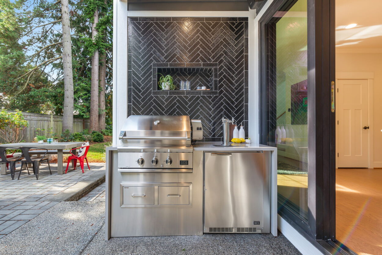 An outdoor kitchen with a grill, fridge, and wine tap on a small patio, perfect for hosting and community gatherings, exemplifying effective and trendy outdoor remodeling.